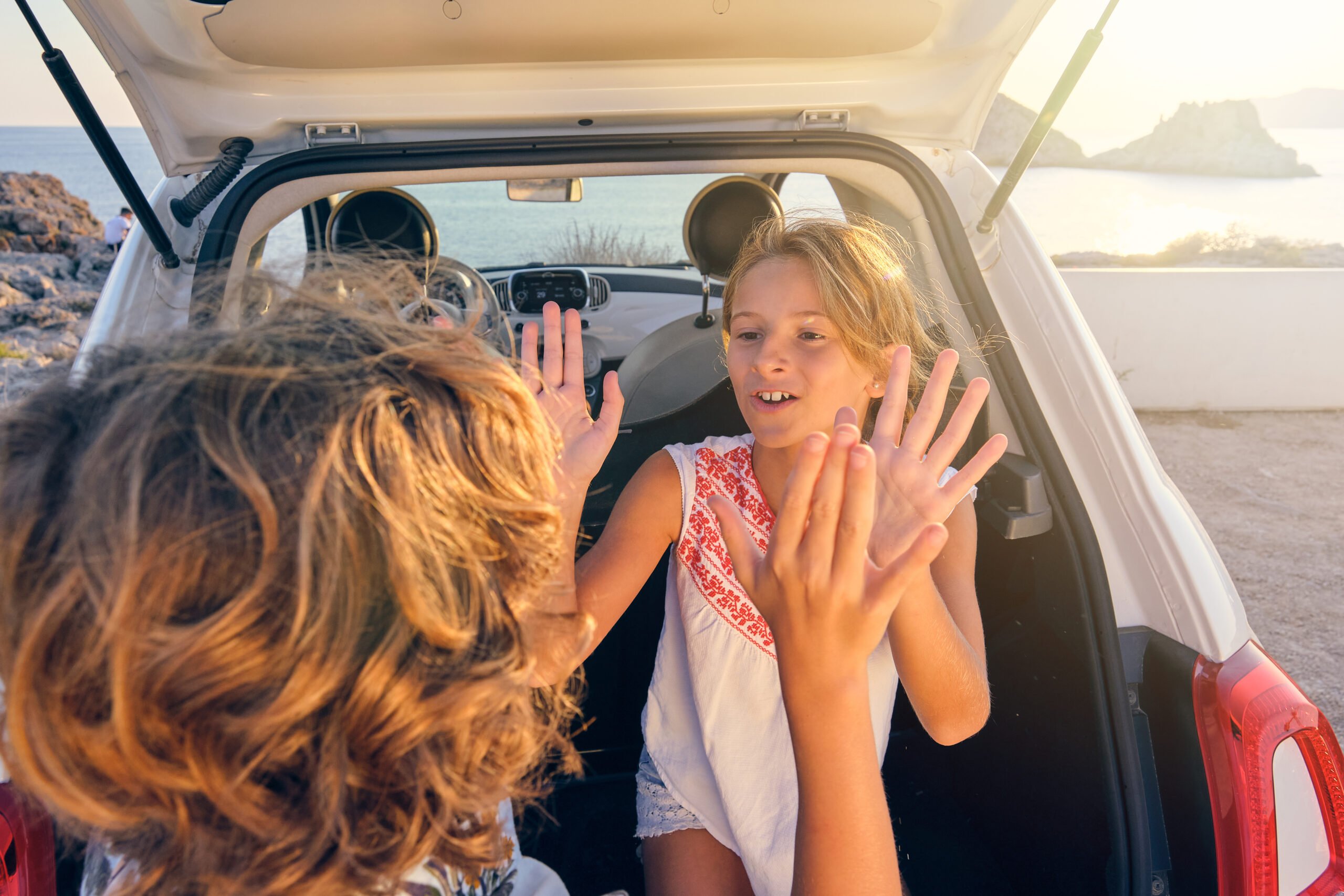 happy siblings summer outfits playing patty cake game near opened car trunk vacation sandy seashore scaled